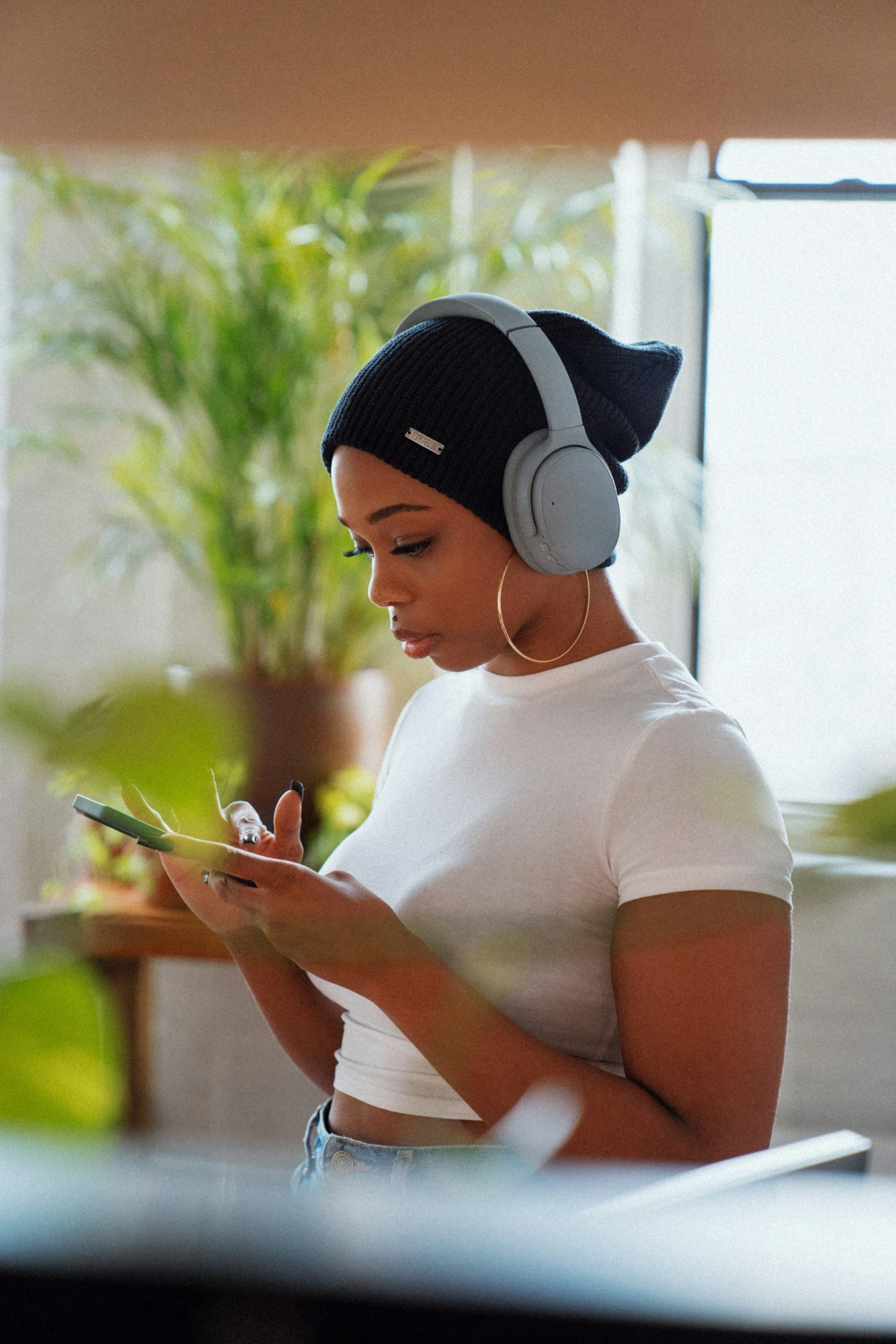 Focused woman with noise-canceling headphones on, blocking out household chaos while checking phone for relaxation tips