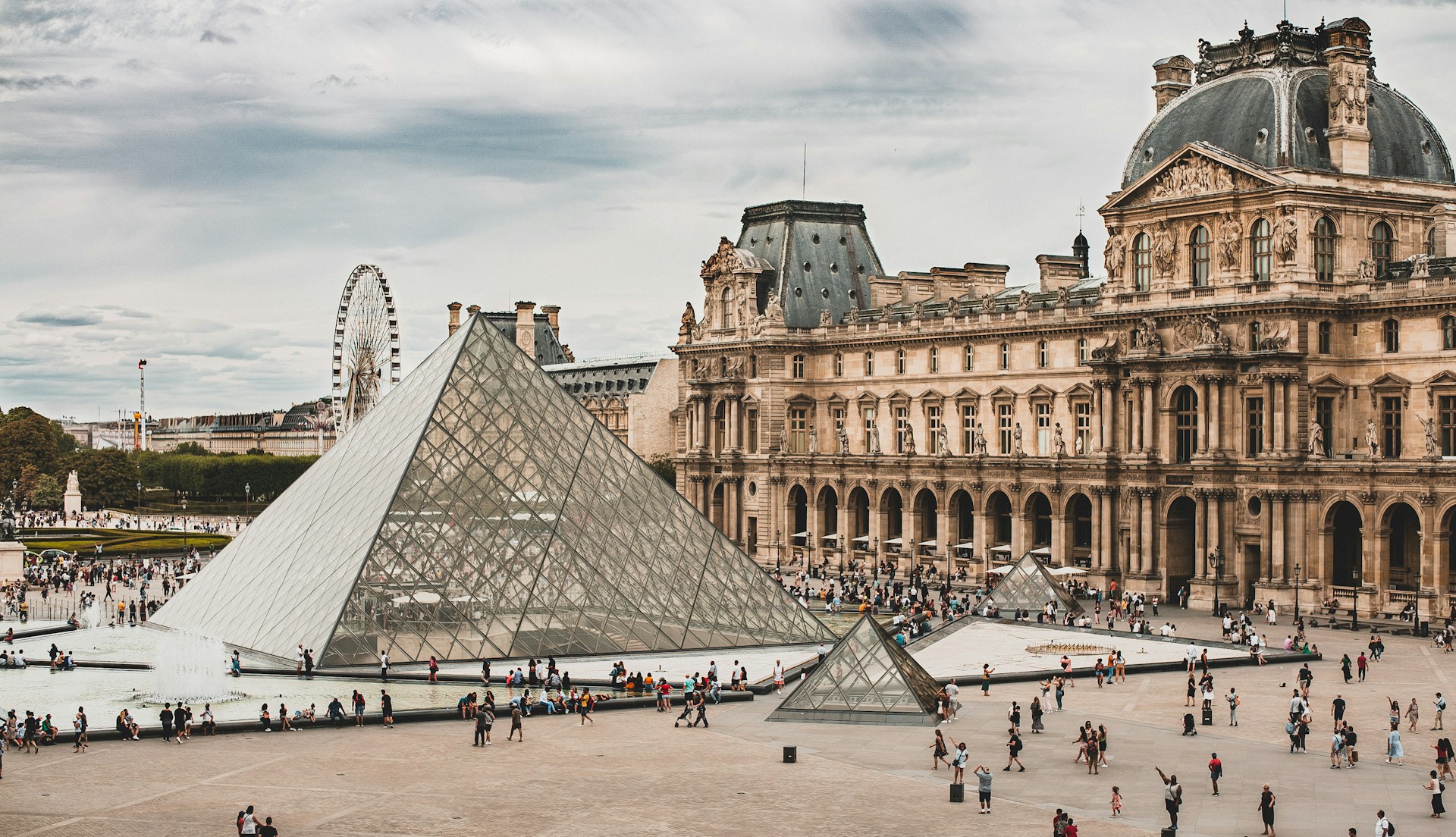 The glass pyramid entrance of the Louvre Museum in Paris with visitors and clear blue sky, iconic Paris landmark and top cultural attraction