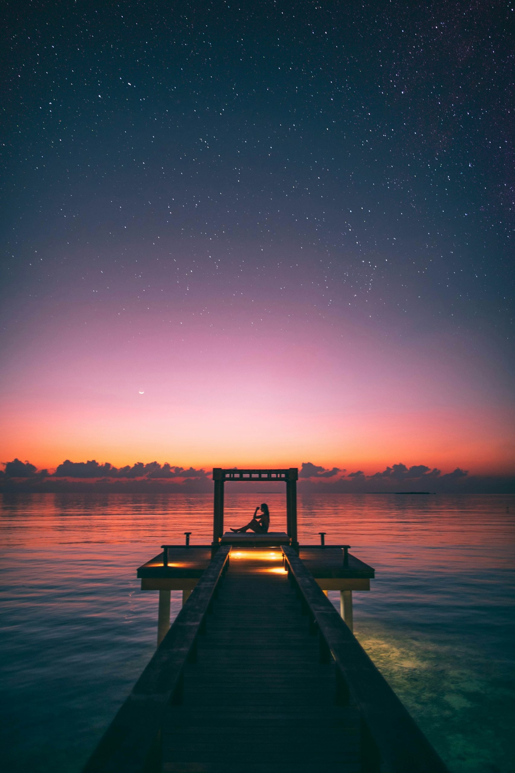 Silhouette of person sitting on a pier during a surreal sunset with stars in the sky, used as an aesthetic TikTok reaction image