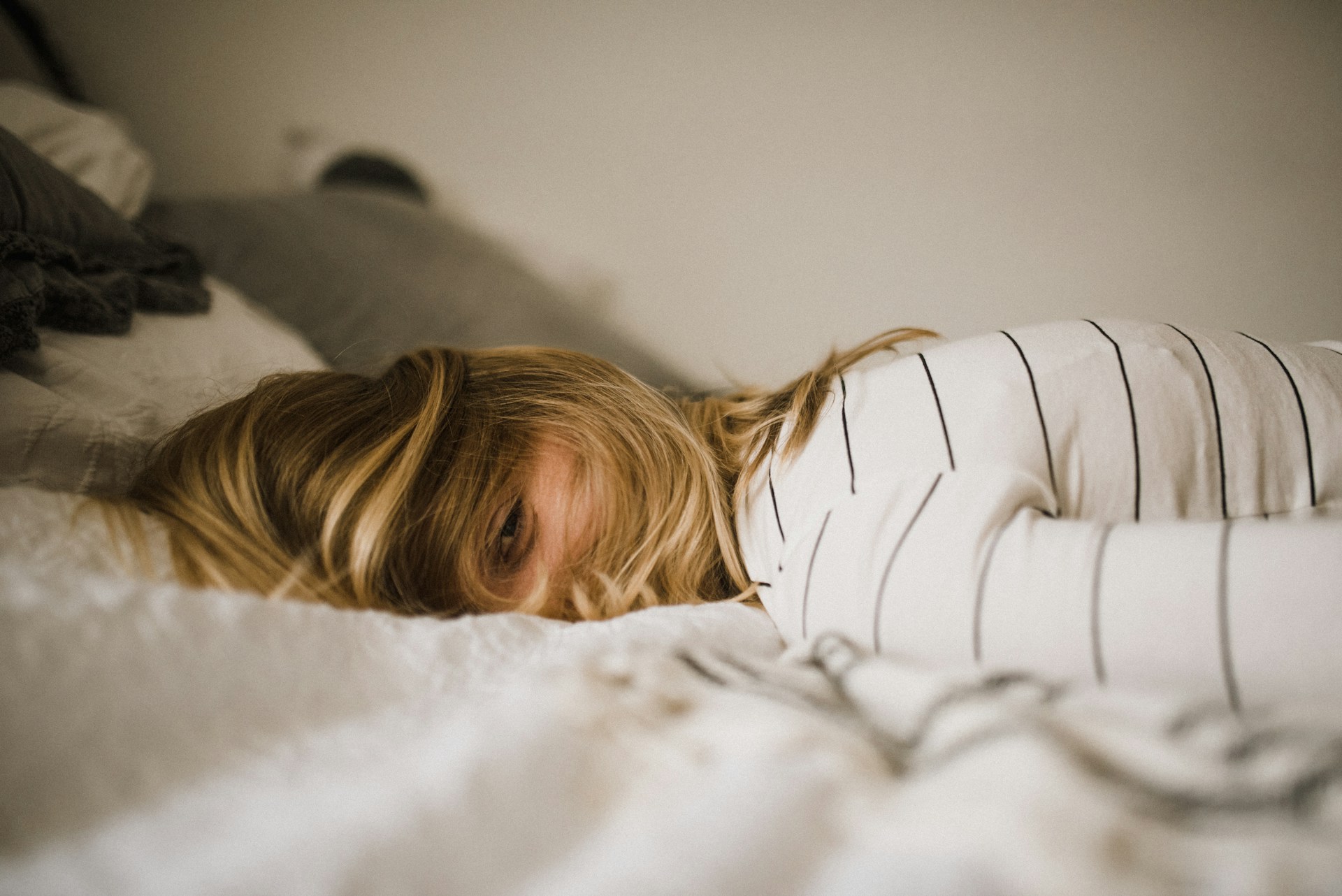 Anxious woman in bed peeking from under hair, representing nightmares or sleep paralysis